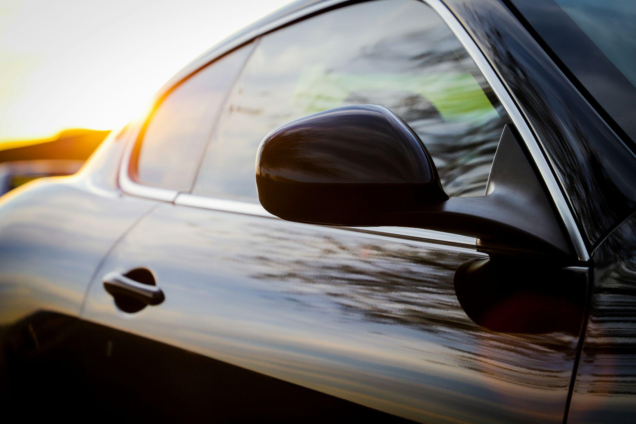 A close-up of a car door and side mirror at sunset, highlighting professional car window tinting in Clovis.